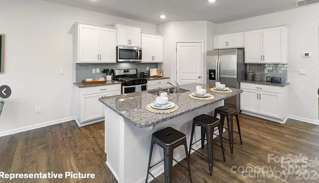 a kitchen with stainless steel appliances granite countertop a stove a refrigerator a sink a dining table and chairs
