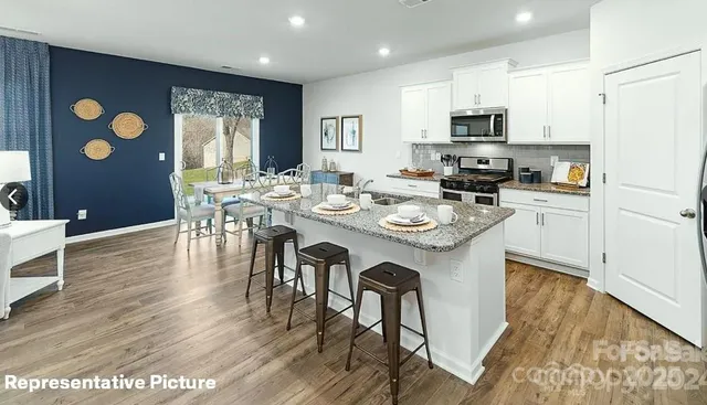 a kitchen with stainless steel appliances granite countertop a stove top oven a sink a dining table and chairs with wooden floor