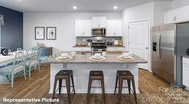 a kitchen with stainless steel appliances granite countertop a dining table chairs refrigerator and microwave