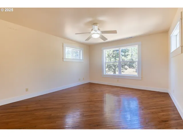 an empty room with wooden floor chandelier fan and windows