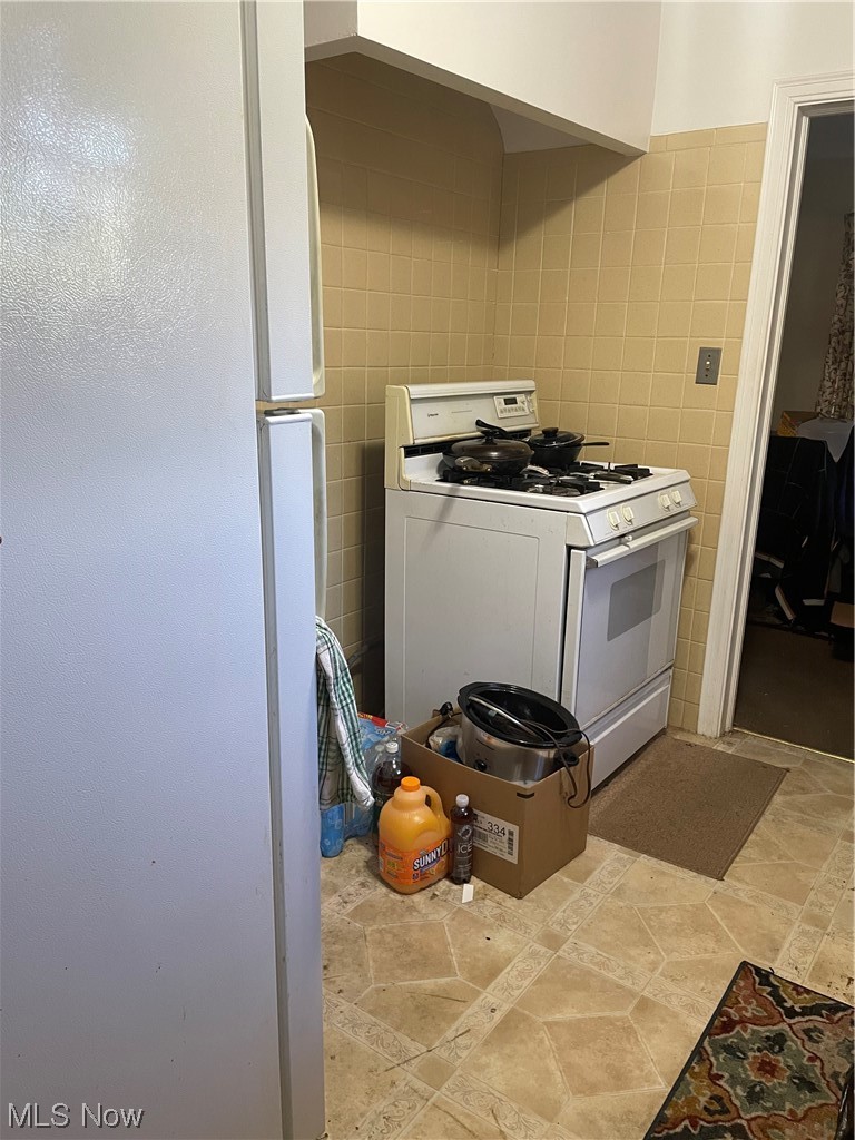 3835 Covington Road Cleveland, OH 44121 - Photo 11 of 34 Kitchen featuring white fridge, tile walls, light tile floors, and stove