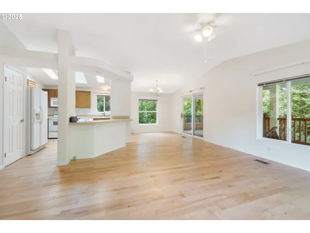 a view of an empty room and kitchen with wooden floor