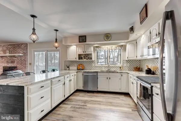 a kitchen with stainless steel appliances kitchen island granite countertop a sink a stove a refrigerator and white cabinets