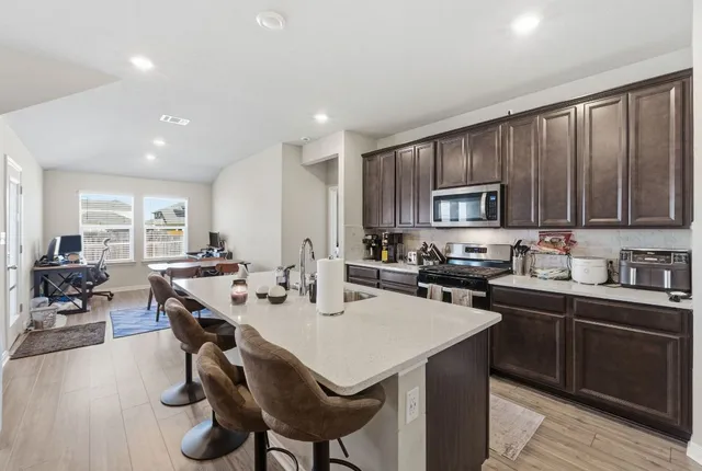 a kitchen with stainless steel appliances a sink a stove a refrigerator cabinets and dining table