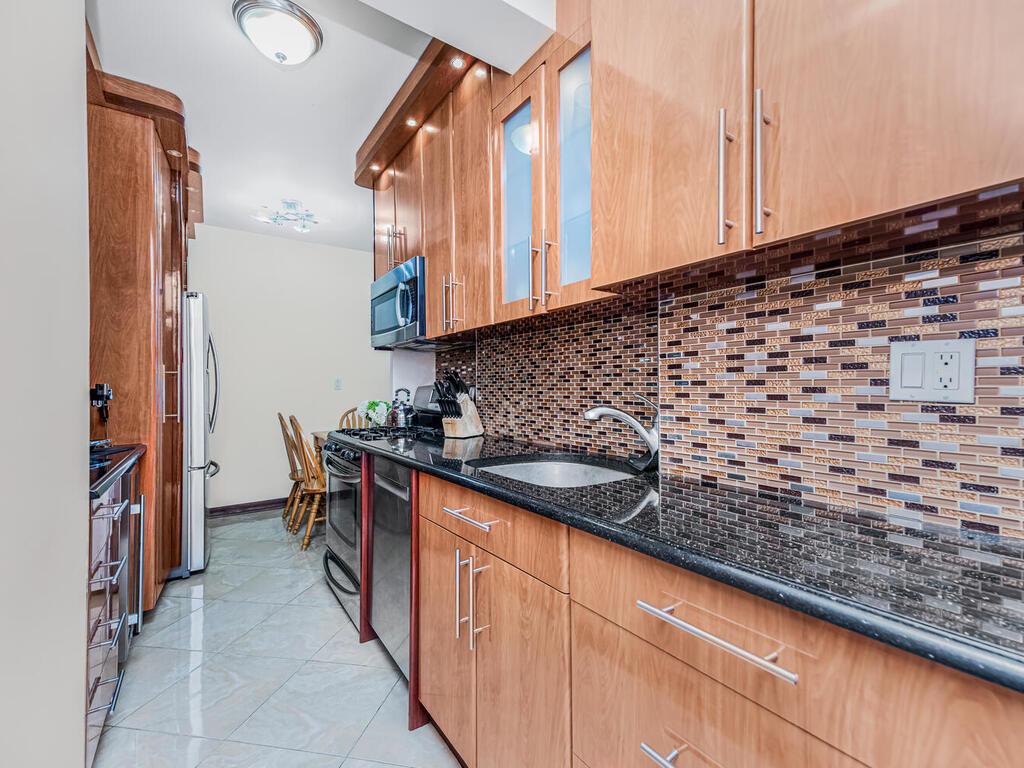 99-60 63rd Road, Unit 14Z Queens, NY 11374 - Photo 1 of 1 Kitchen featuring appliances with stainless steel finishes, sink, backsplash, dark stone countertops, and light tile patterned floors