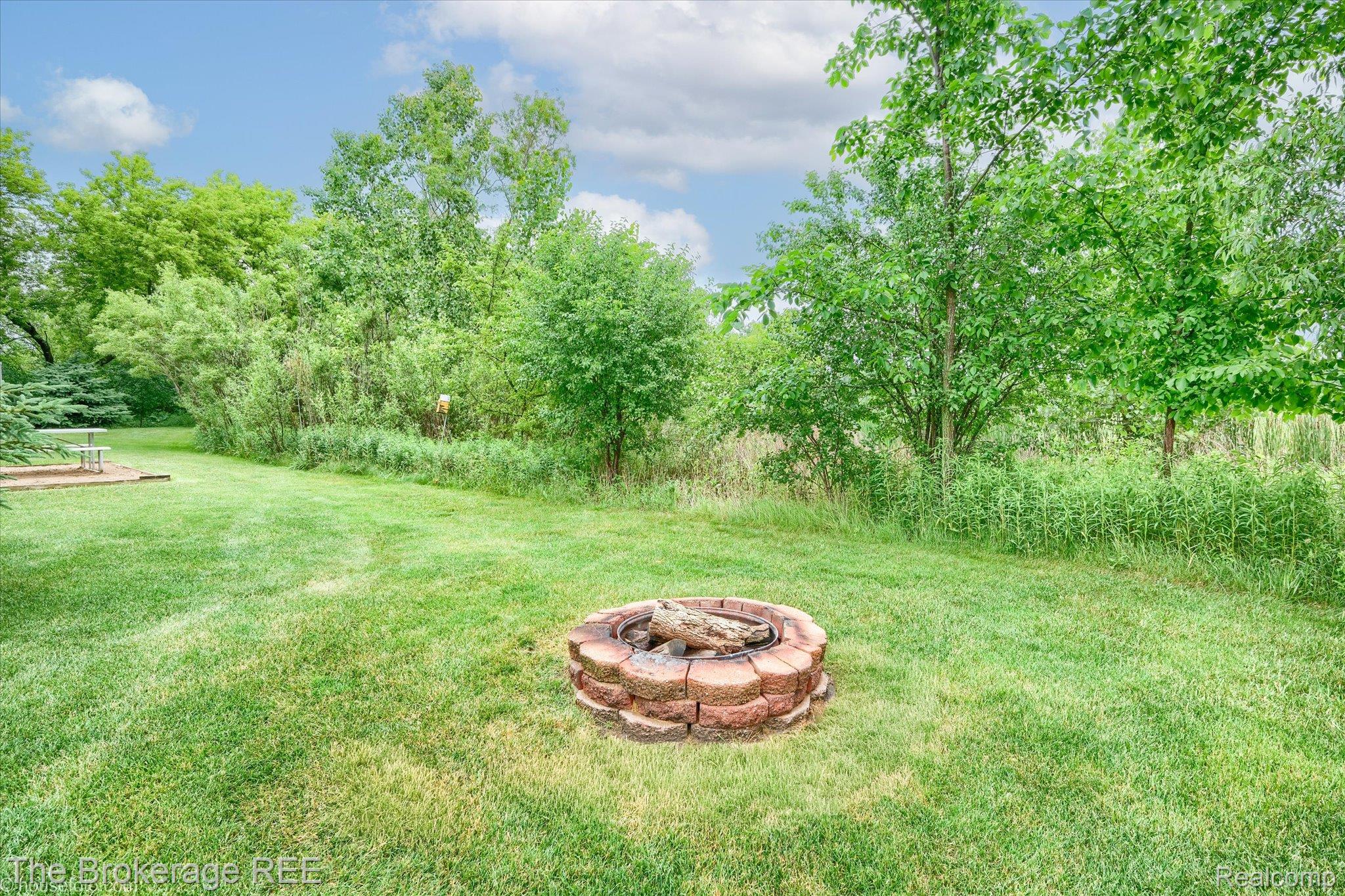4432 North Belsay Road Flint, MI 48506 - Photo 9 of 79 Expansive grassy backyard featuring a brick-ringed fire pit, mature trees, and a concrete patio section