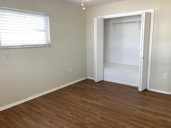 an empty room with wooden floor closet and windows