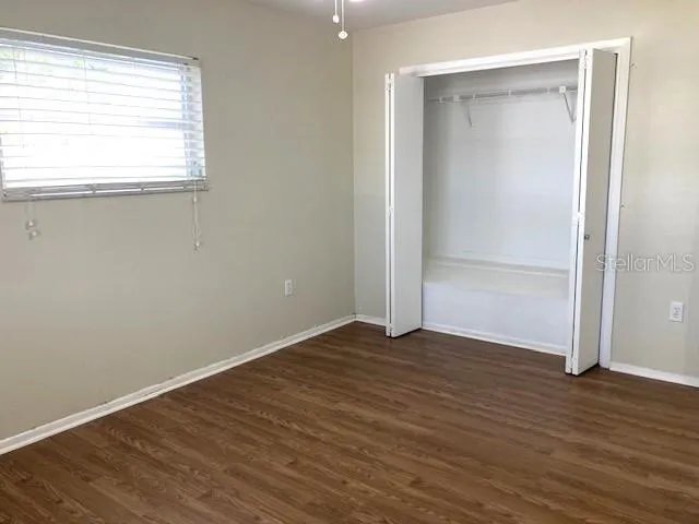 an empty room with wooden floor closet and windows