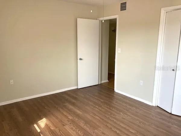 a view of an empty room with wooden floor and closet