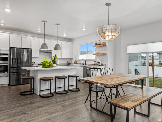 Expansive kitchen featuring a large island with seating, stainless steel appliances, white cabinetry, and wood-finish flooring