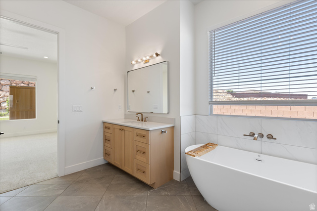1192 East Corral Way Washington, UT 84780 - Photo 29 of 81 Contemporary bathroom featuring a freestanding soaking tub, single vanity with light wood cabinetry, stone countertop, and large format floor tiling