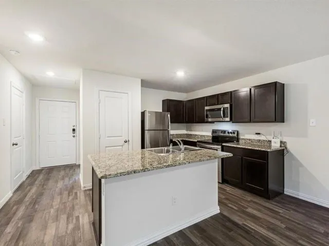 a kitchen with stainless steel appliances granite countertop a stove top oven a sink dishwasher a refrigerator and cabinets with wooden floor