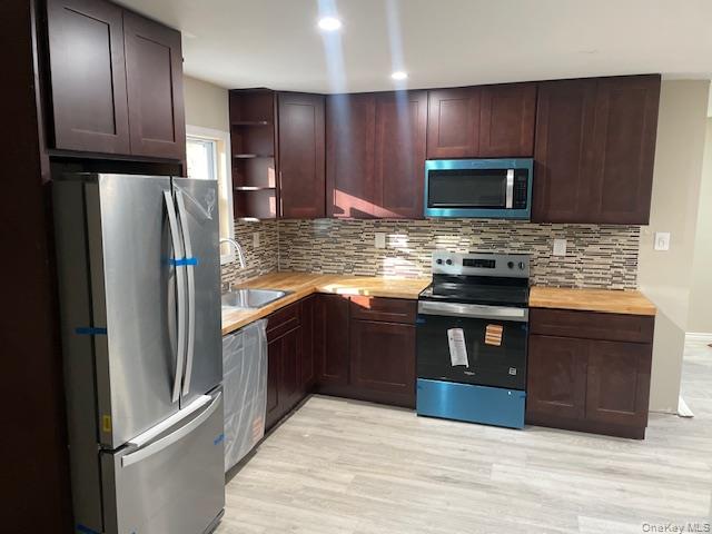 Kitchen with appliances with stainless steel finishes, dark brown cabinetry, backsplash, light wood-type flooring, and open shelves