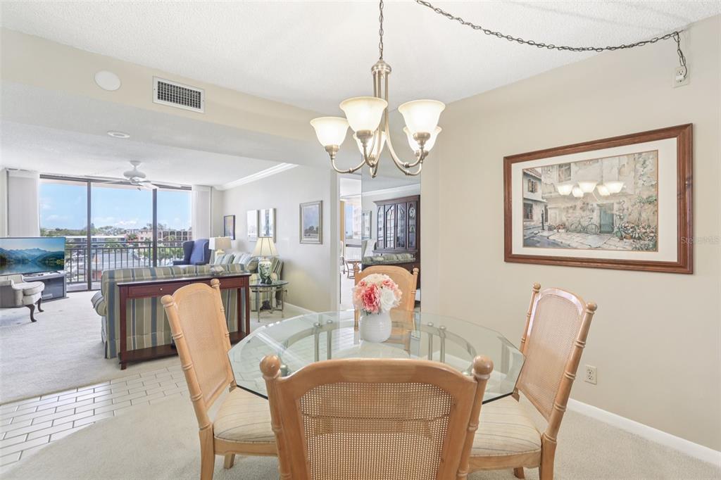 1 Key Capri, Unit 302E Treasure Island, FL 33706 - Photo 7 of 29 a dining room with wooden floor a chandelier a glass table and chairs