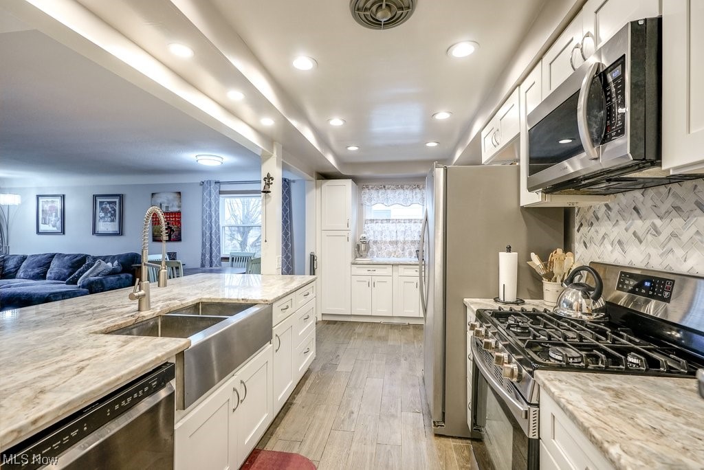 4828 South Sedgewick Road Cleveland, OH 44124 - Photo 2 of 19 Kitchen with light hardwood / wood-style flooring, white cabinetry, light stone countertops, stainless steel appliances, and backsplash