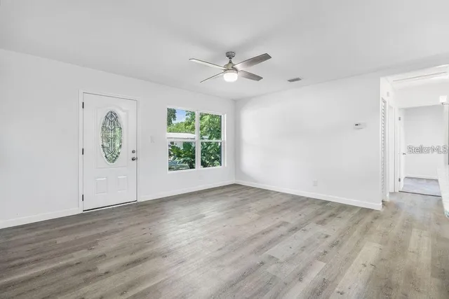 an empty room with wooden floor chandelier fan and windows
