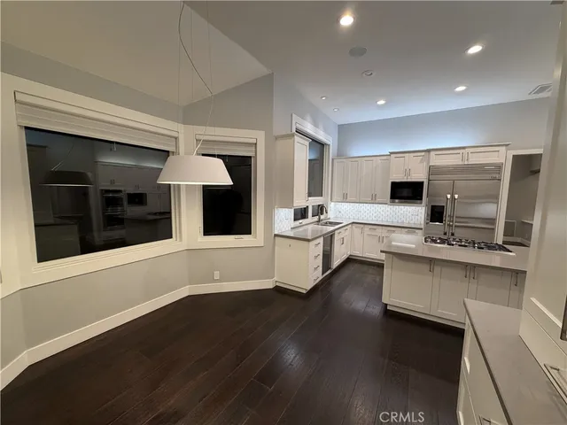 a large white kitchen with a white countertops a stove a fireplace and a dining table with wooden floor