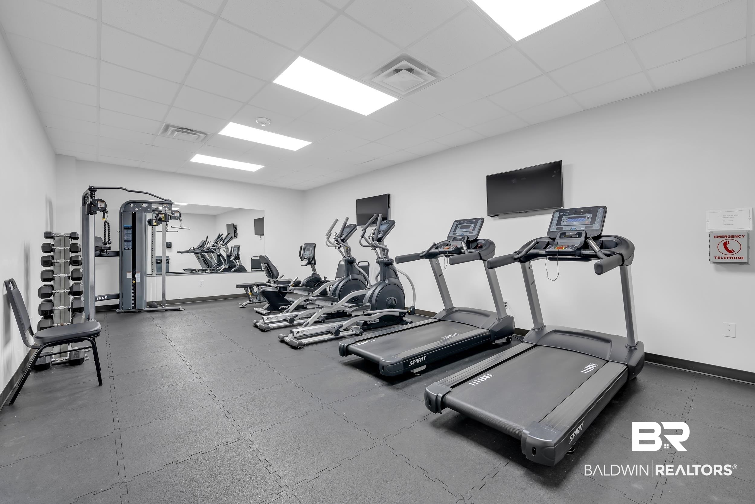 400 Plantation Road, Unit 2118 Gulf Shores, AL 36542 - Photo 35 of 59 Dedicated fitness area featuring durable rubber mat flooring, wall-mounted televisions, a selection of cardio equipment including treadmills and ellipticals, a multi-station weight machine, and a dumbbell rack