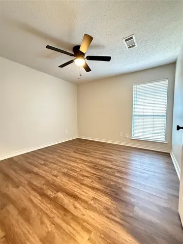 an empty room with wooden floor ceiling fan and windows