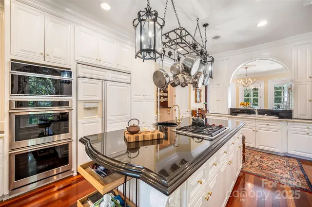 a kitchen with stainless steel appliances granite countertop a stove a refrigerator a kitchen island a sink dishwasher a dining table and chairs with wooden floor