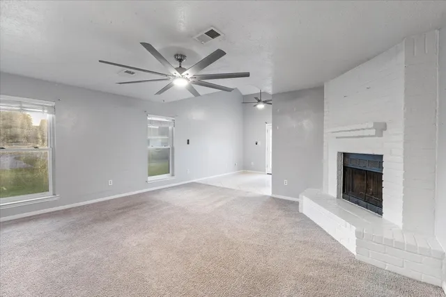 an empty room with windows fireplace and fan
