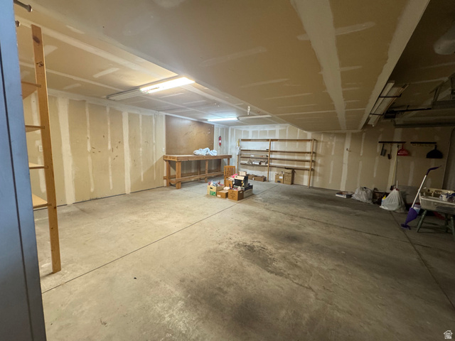 88 Canterbury Lane Logan, UT 84321 - Photo 31 of 37 Spacious garage featuring a concrete floor, exposed wall studs, built-in wooden shelving, a wooden workbench, and fluorescent overhead lighting