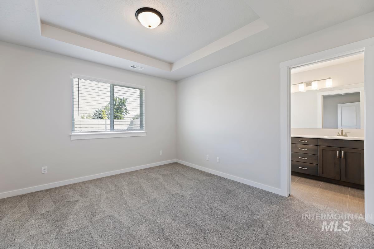 212 East Radiant Ridge Drive Meridian, ID 83642 - Photo 15 of 36 Unfurnished bedroom featuring light colored carpet, ensuite bathroom, and a raised ceiling
