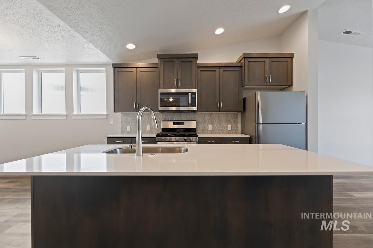 212 East Radiant Ridge Drive Meridian, ID 83642 - Photo 5 of 36 Kitchen with light wood-type flooring, dark wood finish cabinetry, stainless steel appliances, a center island with sink, and backsplash