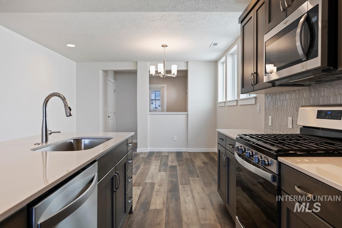 212 East Radiant Ridge Drive Meridian, ID 83642 - Photo 8 of 36 Kitchen featuring stainless steel appliances, dark wood-style floors, decorative backsplash, a chandelier, and a textured ceiling
