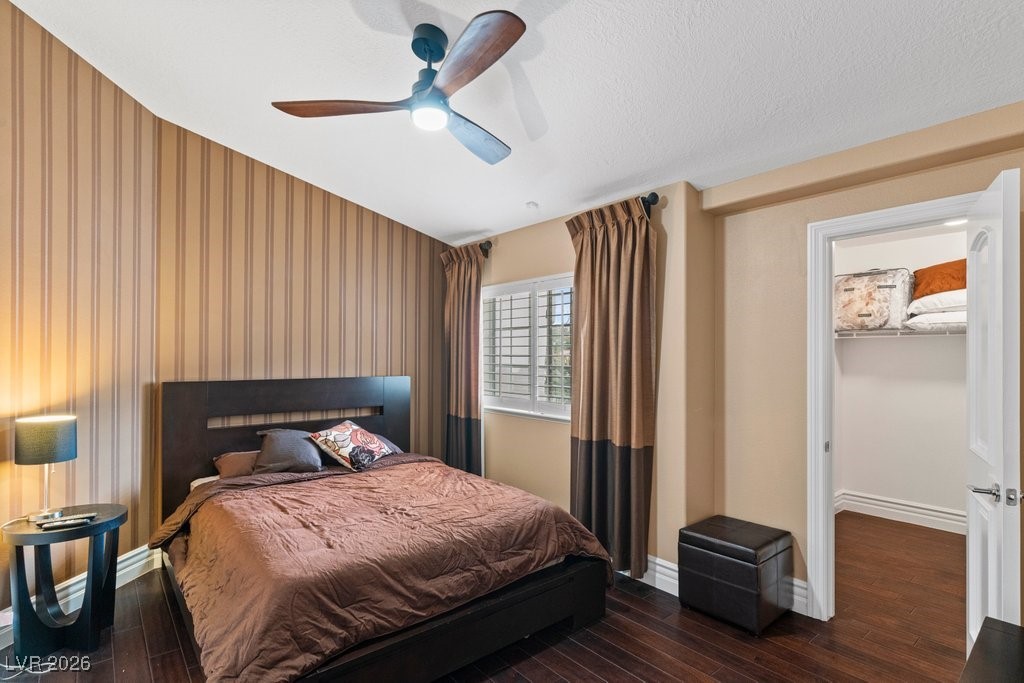 7 Larkside Court Henderson, NV 89014 - Photo 47 of 70 Bedroom featuring dark wood finished floors, ceiling fan, a walk in closet, wallpapered walls, and a textured ceiling