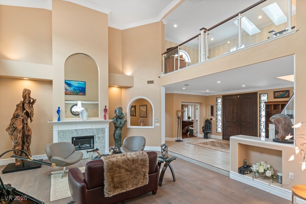 7 Larkside Court Henderson, NV 89014 - Photo 10 of 70 Living area with ornamental molding, a high ceiling, wood finished floors, a premium fireplace, and a skylight