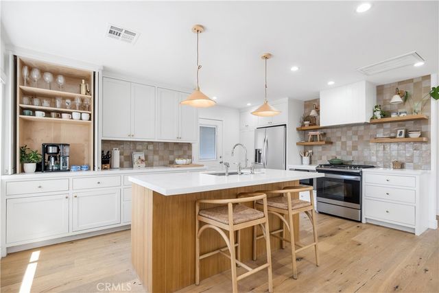 a kitchen with a stove a sink a kitchen island with chairs and cabinets