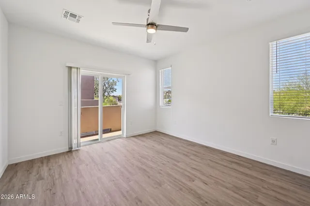 an empty room with wooden floor ceiling fan and windows