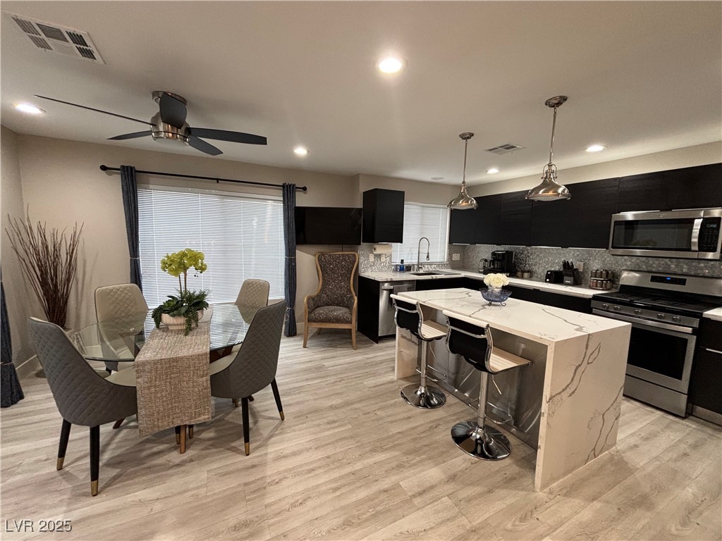 Kitchen with dark cabinets, appliances with stainless steel finishes, decorative light fixtures, decorative backsplash, and a kitchen island