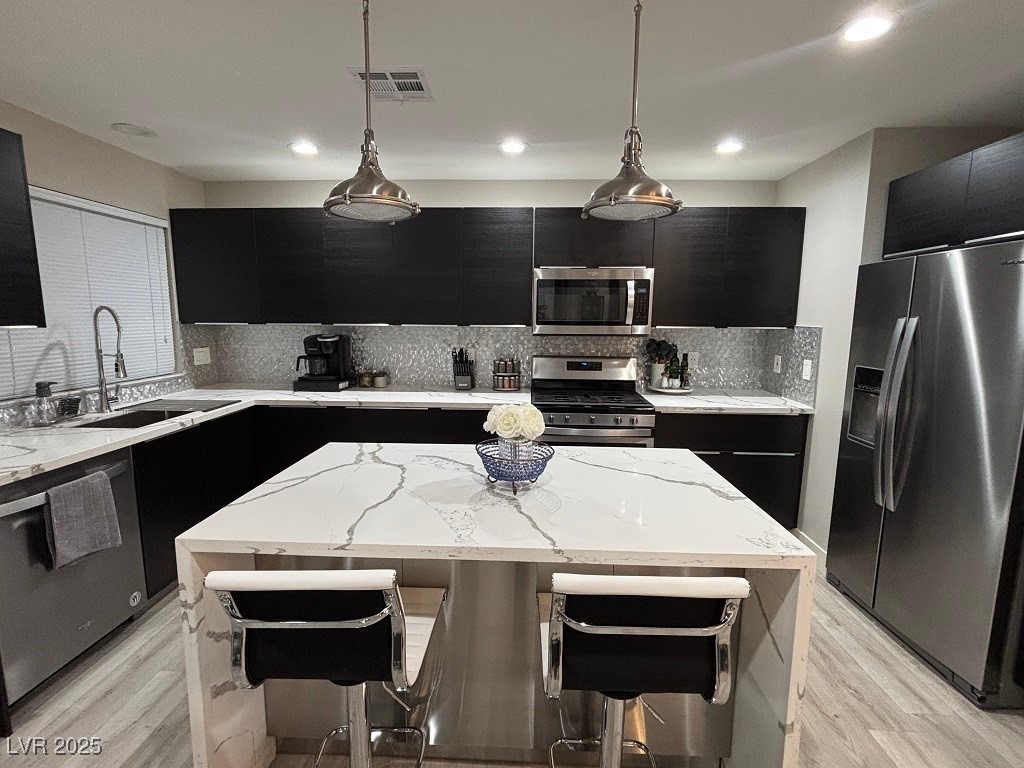 2784 Fountain Ridge Lane Henderson, NV 89074 - Photo 3 of 37 Kitchen with dark cabinets, light stone counters, a breakfast bar area, a center island, and hanging light fixtures