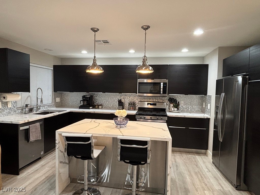 2784 Fountain Ridge Lane Henderson, NV 89074 - Photo 4 of 37 Kitchen with dark cabinetry, light stone countertops, a kitchen bar, appliances with stainless steel finishes, and decorative light fixtures