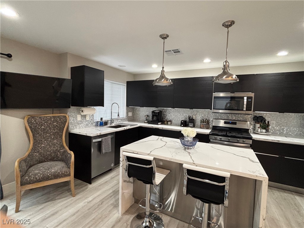 2784 Fountain Ridge Lane Henderson, NV 89074 - Photo 8 of 37 Kitchen featuring dark cabinetry, light stone countertops, tasteful backsplash, stainless steel appliances, and decorative light fixtures