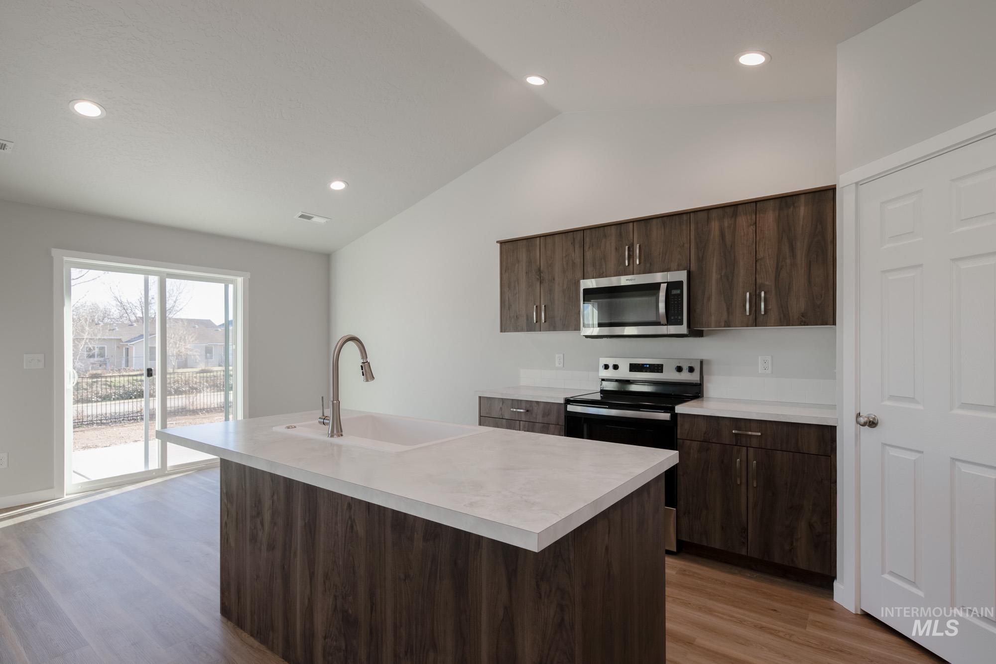 3290 South Maple Rnch Way Nampa, ID 83686 - Photo 6 of 20 Kitchen featuring dark brown cabinetry, light countertops, an island with sink, vaulted ceiling, and stainless steel microwave