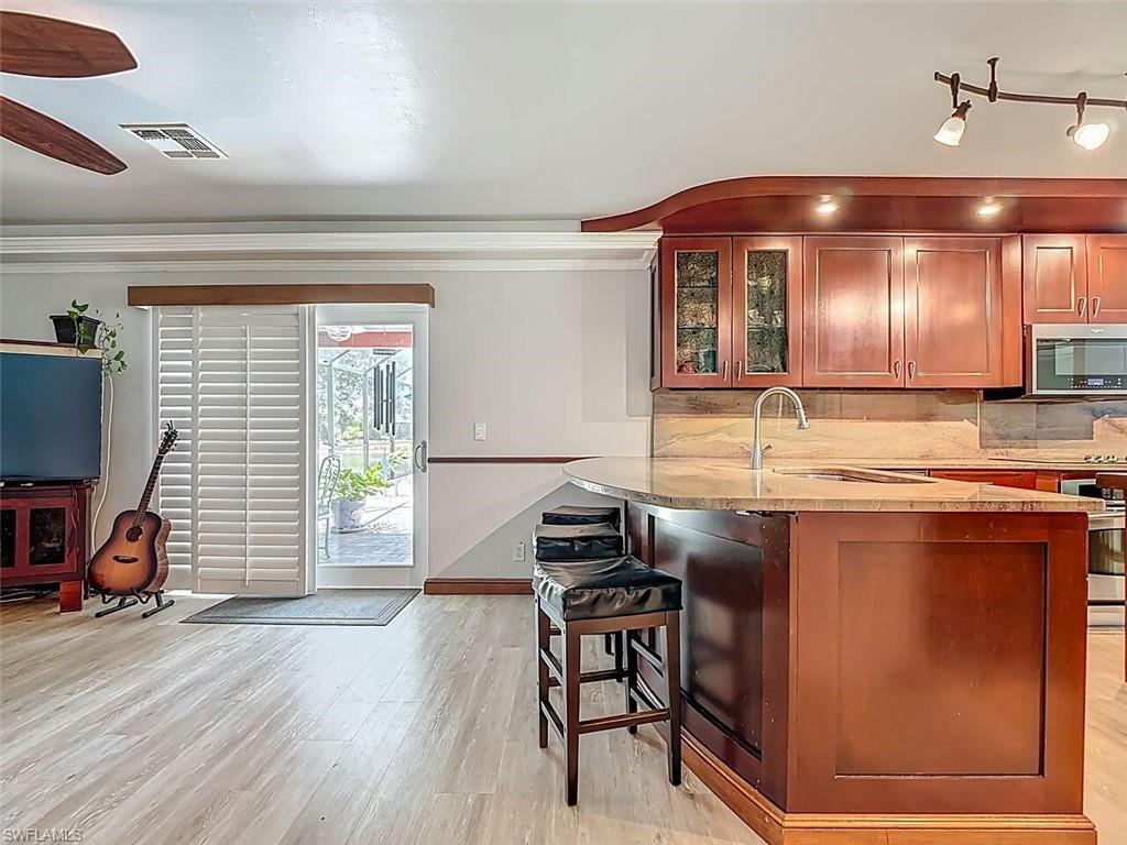 14991 Savannah Drive Naples, FL 34119 - Photo 19 of 50 a kitchen with stainless steel appliances granite countertop a sink dishwasher a stove and a dining table with wooden floor