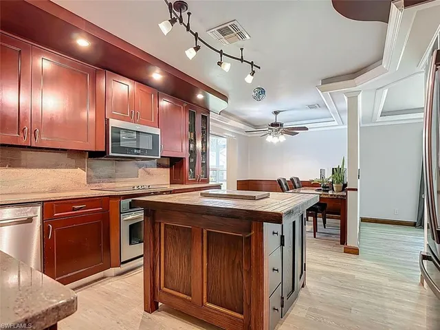 a kitchen with stainless steel appliances granite countertop wooden cabinets a sink dishwasher a stove and a refrigerator with wooden floor