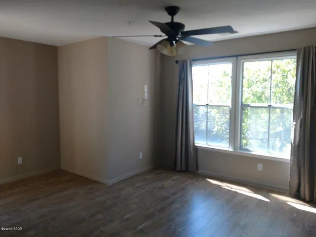 an empty room with wooden floor fan and windows