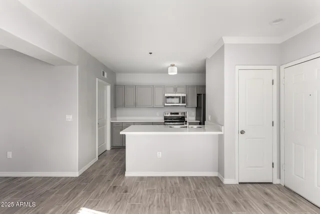 a living room with stainless steel appliances a wooden floor a large window and a sink