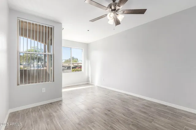 an empty room with wooden floor fan and windows