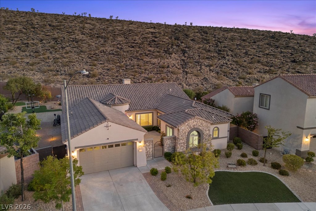 2125 De Rouge Avenue Henderson, NV 89044 - Photo 87 of 96 A spacious desert home features a paver driveway, stone accents, and a tile roof, nestled against a natural hill.