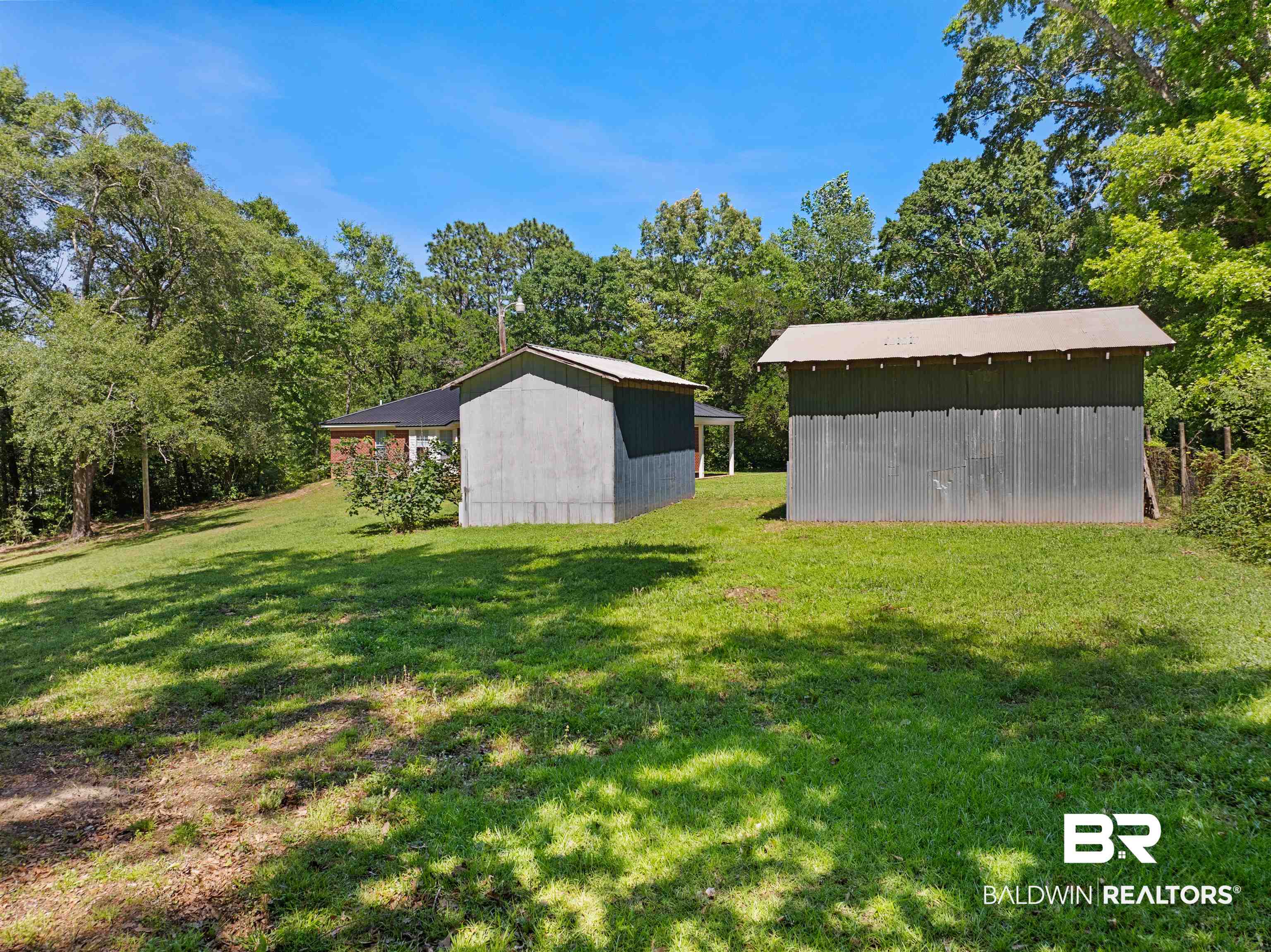 35893 Pine Road South Stapleton, AL 36578 - Photo 31 of 31 Expansive green lawn featuring two outbuildings with corrugated metal siding and a partially visible brick residence surrounded by mature trees