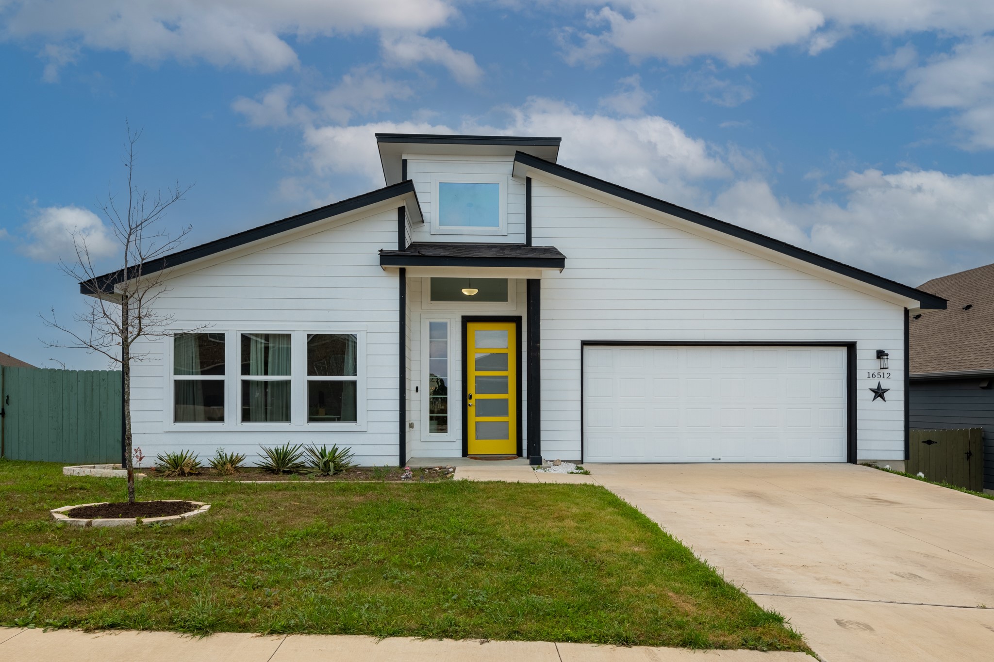 Mid-century inspired home featuring an attached garage, concrete driveway, a front lawn, and fence