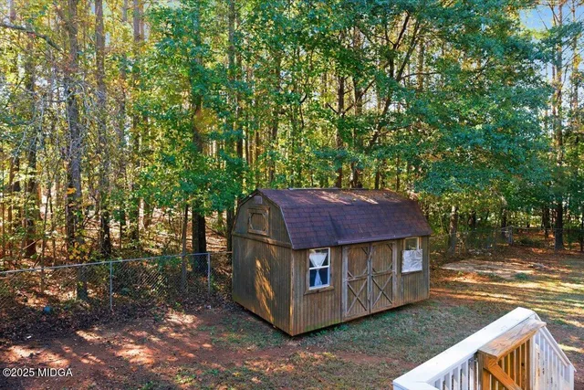 a view of a small yard in front of a house with large trees and wooden fence