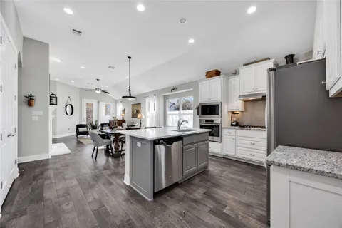 a kitchen with stainless steel appliances kitchen island granite countertop a refrigerator a stove top oven a sink dishwasher and white cabinets with wooden floor