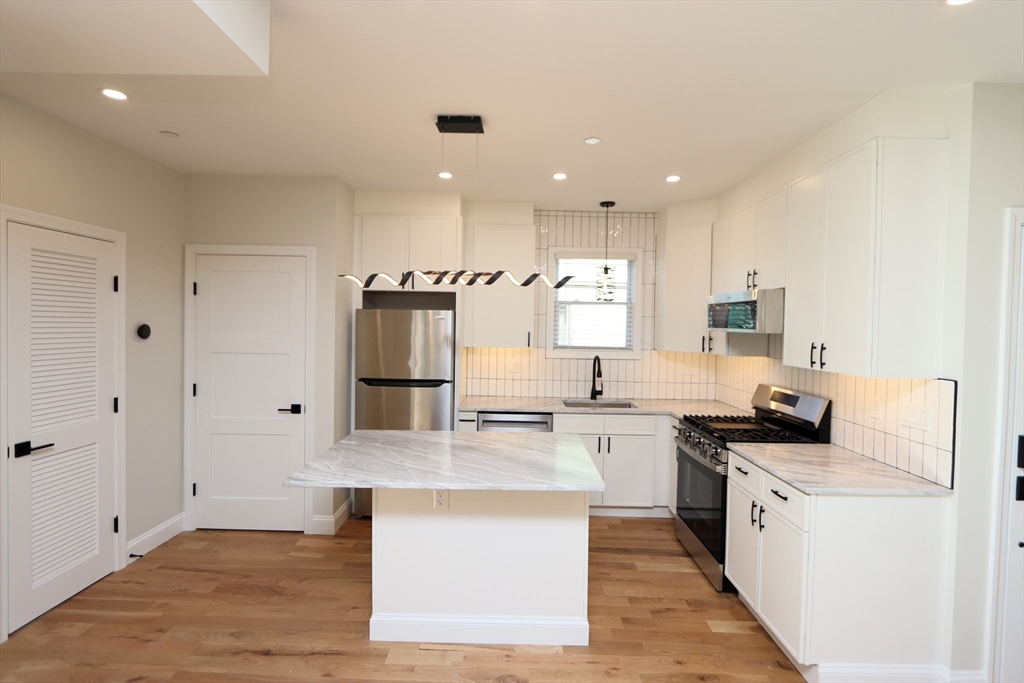14-16 Harriet Street, Unit 1 Boston, MA 02135 - Photo 2 of 28 a large kitchen with stainless steel appliances granite countertop a stove top oven a sink and white cabinets