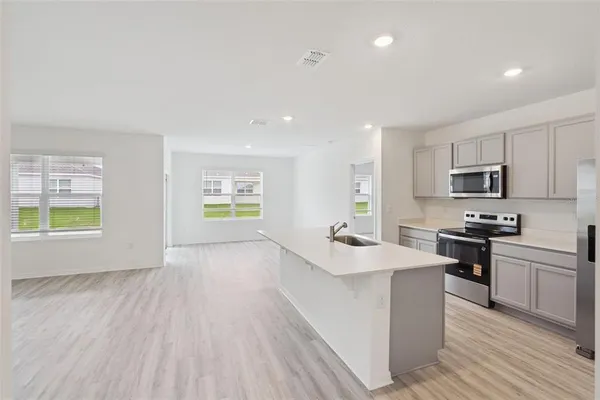 a kitchen with stainless steel appliances a stove a sink a refrigerator white cabinets and wooden floor